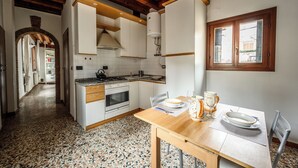 Cuina amb armaris blancs, sostre de fusta, sòl de rajola i zona de menjador amb taula preparada per a dues persones.