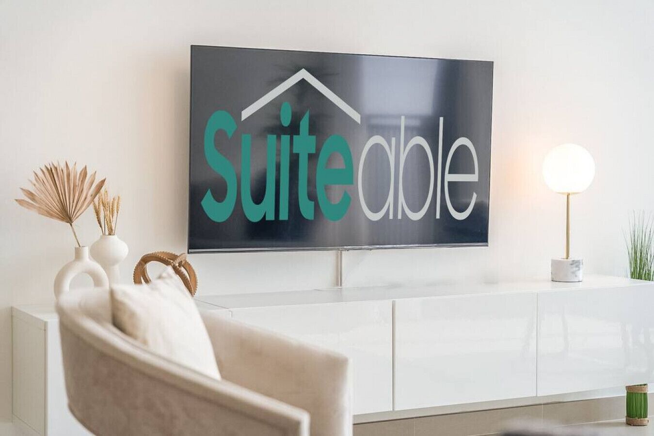 A modern living room with a large flat-screen TV mounted on the wall displaying the text 'SuiteAble.'