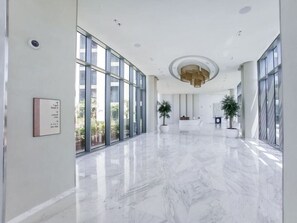 A spacious lobby with a marble floor, large windows, and potted plants.