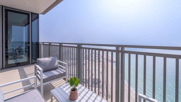 A balcony with a view of the sea, a table with a plant, and a sofa with cushions. - Sunset spot with breathtaking view by Suiteable (Dubai)
