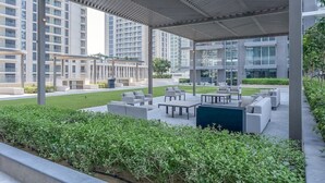 A covered outdoor seating area with modern furniture, surrounded by greenery and high-rise buildings in the background. - Your beachfront luxe escape experience - Suiteable (Dubai)