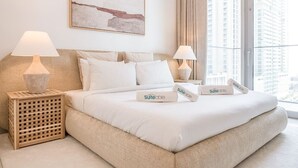 Ein Hotelzimmer mit einem großen Bett, zwei Nachttischen mit Lampen, Blick auf hohe Gebäude durch große Fenster und einem abstrakten Kunstwerk an der Wand.