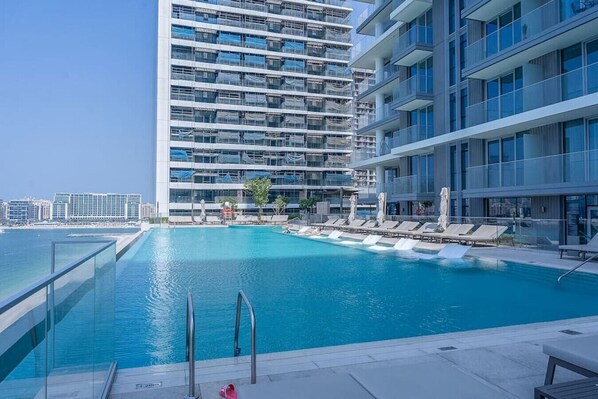 A modern hotel with a rooftop infinity pool, lounge chairs, and a clear view of the city skyline.