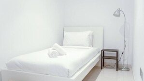 A minimalist bedroom with a white bed, a bedside table, and a floor lamp. - Your beachfront luxe escape experience - Suiteable (Dubai)