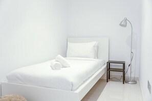 A minimalist bedroom with a white bed, a bedside table, and a floor lamp.