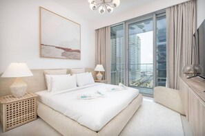 A modern hotel room with a large bed, two bedside tables with lamps, a view of tall buildings through floor-to-ceiling windows, and a minimalist decor.