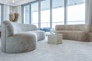 Uma sala de estar moderna com dois sofás cinza, uma mesa de centro de mármore e amplas janelas com vista para a cidade.