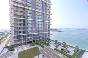 A high-rise residential building with balconies, a view of the sea, and a landscaped courtyard.