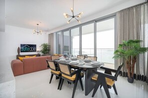 Un espace de repas moderne avec une table ronde pour quatre personnes, un canapé et une grande fenêtre agrémentée de rideaux.