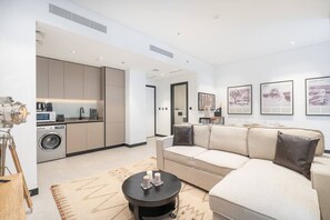 Una sala de estar moderna con un sofá color beige, una mesa de centro y una zona de cocina con electrodomésticos.