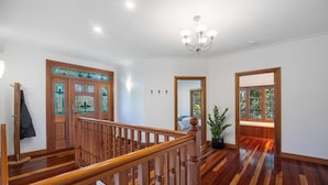 Un pasillo amplio con una escalera de madera, un candelabro y un ventanal con vistas a la vegetación.