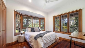 Un dormitorio con una cama grande, suelo de madera y ventanas amplias con marcos de madera.