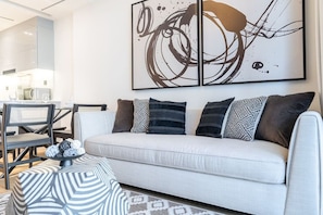 Una sala moderna con un sofá, almohadones estampados, una mesita de centro con ovillos de lana y un cuadro abstracto grande en la pared.