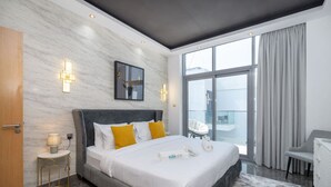 A modern hotel room with a large bed, a small bedside table, a chair, and a view of the city through large windows. - Modern Comfort in a Spacious Apartment - Suiteable (دبي)