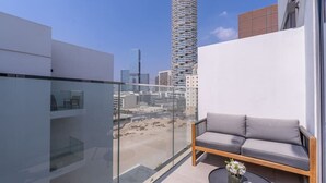 A balcony with a sofa and a small table, overlooking a cityscape with modern buildings. - Modern Comfort in a Spacious Apartment - Suiteable (دبي)