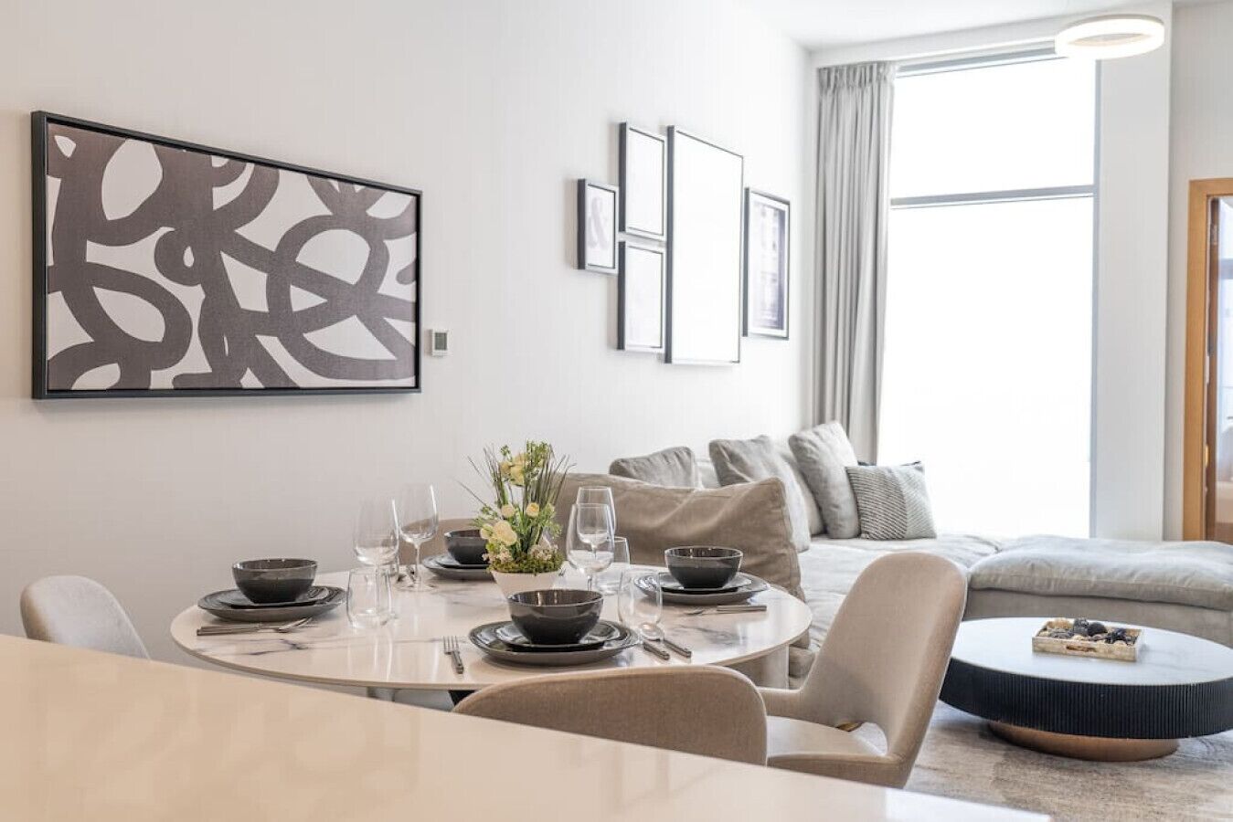 Ein modernes Wohnzimmer mit Essbereich, mit einem runden Tisch für vier Personen, einer Couch und einem Couchtisch.