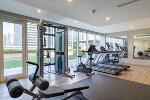A modern gym with cardio machines, weightlifting equipment, and large windows offering city views. - Business Bay Bliss 1 bedroom apartment - Suiteable (Dubai)