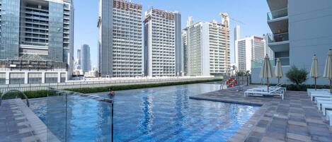 A rooftop pool with clear blue water, surrounded by modern buildings and a clear sky.
