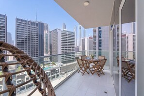 A balcony with a table and chairs, overlooking a cityscape with modern buildings.