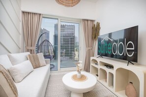 A modern living room with a sofa, a TV, and a glass door leading to a balcony. - Business Bay Bliss 1 bedroom apartment - Suiteable (Dubai)