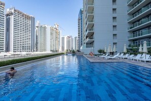 Ein Swimmingpool mit Liegestühlen und Sonnenschirmen, umgeben von Hochhäusern.