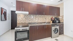 A compact kitchen with dark wooden cabinets, a built-in stove, a washing machine, and a tiled backsplash. - Comfortable Broad Studio in Business Bay-Suiteable (Dubai)
