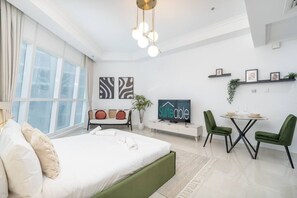 A modern hotel room with a large bed, a desk, a television, and a dining area with chairs.
