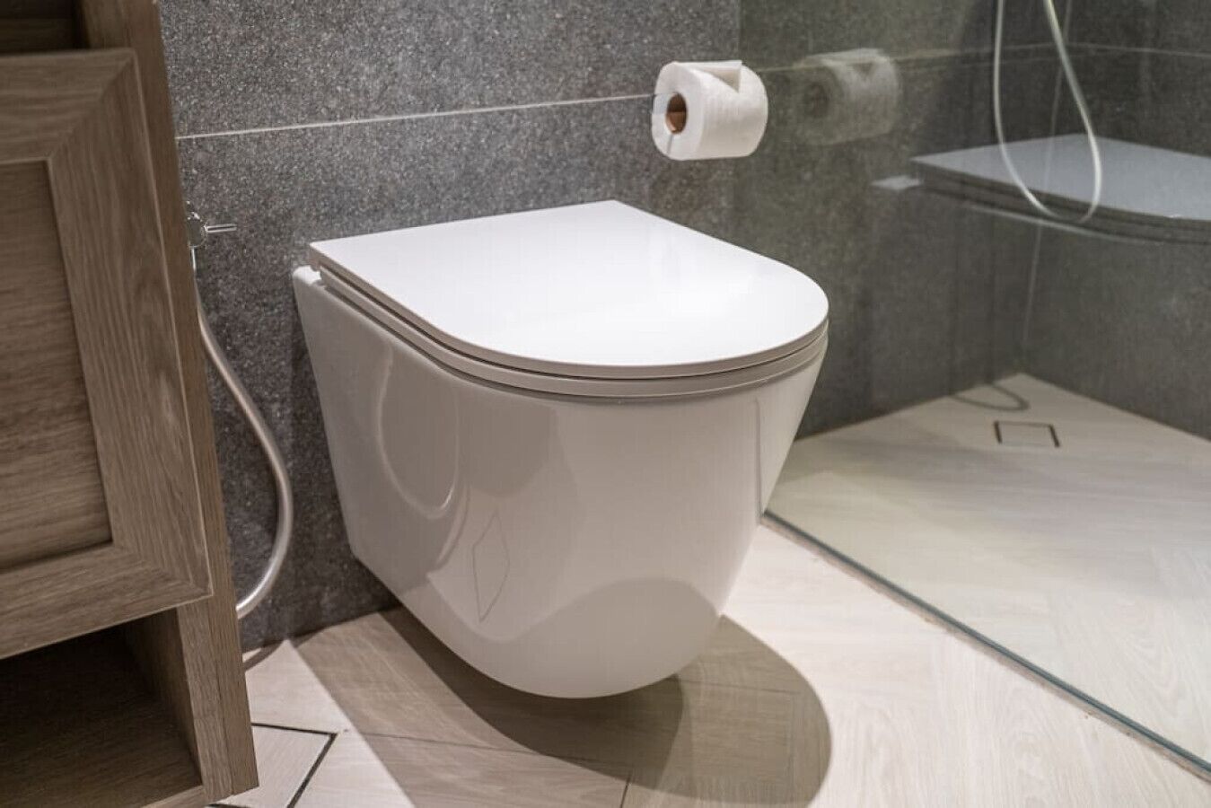 Un baño moderno con inodoro blanco, zona de ducha y mueble de madera.