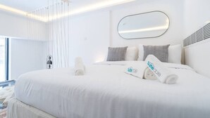 Una habitación de hotel moderna con una cama grande, ropa de cama blanca y un espejo grande encima.