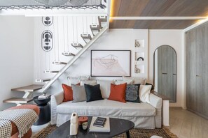A modern living room with a white sofa, a coffee table, and a staircase with a unique design. - Fashionable loft with catamaran net in JVC (Dubai)