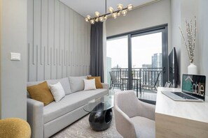 A modern living room with a grey sofa, a glass coffee table, and a laptop on a desk.