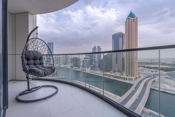 A balcony with a view of a city skyline, a hanging chair, and a glass railing.