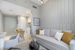 A modern living room with a grey sofa, a glass coffee table, and a dining area with a small table and chairs.