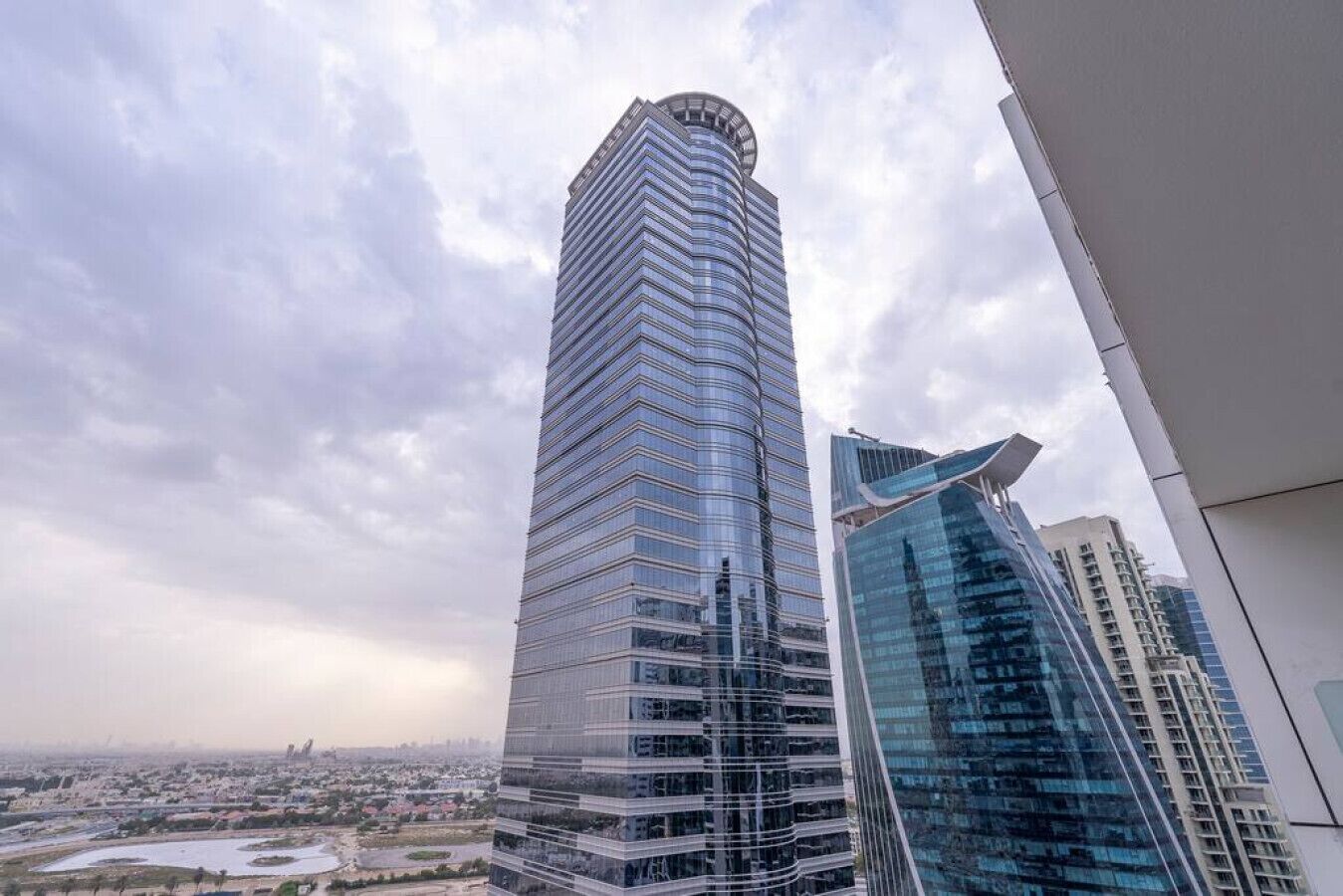 Un edificio de gran altura con un diseño curvo, rodeado de otros edificios modernos y un paisaje urbano al fondo.