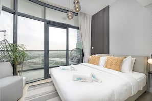 A modern hotel room with a large bed, a view of the city, and a balcony with a plant.