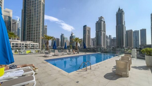 A rooftop pool with lounge chairs and umbrellas, surrounded by high-rise buildings.
