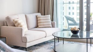A modern living room with a sofa, two pillows, a glass coffee table, and a view of a cityscape through large windows.