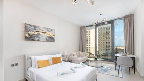 A modern hotel room with a large bed, a sofa, a dining table, and a balcony with a city view.