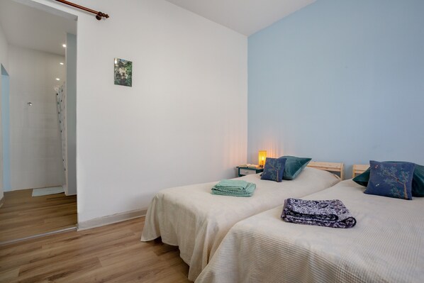 A bedroom with two beds, a nightstand, a wall-mounted lamp, and a door leading to a bathroom.