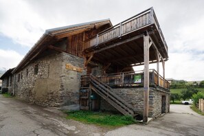A rustic stone building with a wooden balcony and a staircase leading to an upper level.