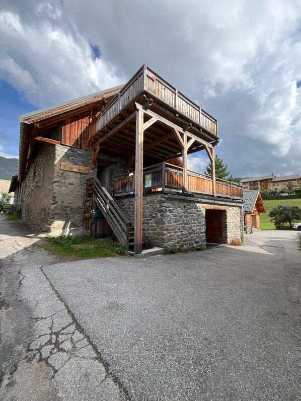 A rustic chalet with a wooden balcony, stone walls, and a staircase leading to the entrance.