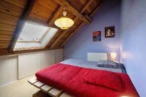 A bedroom with a sloped ceiling, a skylight, a bed with red and grey bedding, a bedside lamp, and two posters on the wall.