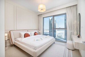 A modern hotel room with a large bed, a nightstand, a bedside table, a mirror, and a view of the city through large windows.