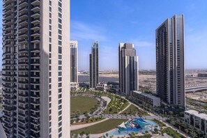 A high-rise residential building with multiple balconies, a swimming pool, and a landscaped area with palm trees.
