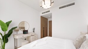 Ein modernes Schlafzimmer mit einem großen Bett, einem Schminktisch mit Spiegel, einer Topfpflanze und einer Tür zu einem anderen Raum.
