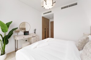 A modern bedroom with a large bed, a vanity with a mirror, a potted plant, and a door leading to another room.