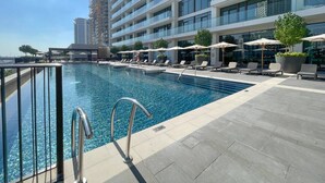Ein Pool auf dem Dach mit Liegestühlen und Sonnenschirmen, umgeben von einem modernen, mehrstöckigen Gebäude.