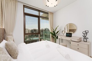 Ein Hotelzimmer mit einem großen Bett, einem Schreibtisch mit Spiegel, einem Schild mit der Aufschrift 'suiteable' und Blick auf die Stadt durch große Fenster.