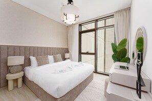 A modern hotel room with a large bed, a desk with a laptop, a mirror, and a large window with curtains.