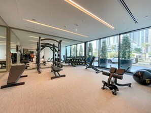 A modern gym with various exercise equipment, large windows, and a view of the city.